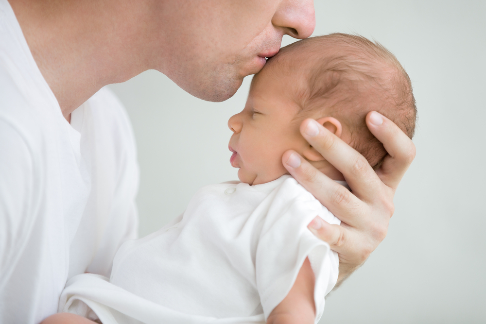 close-up portrait of happy young father hugging and kissing his sweet adorable newborn child